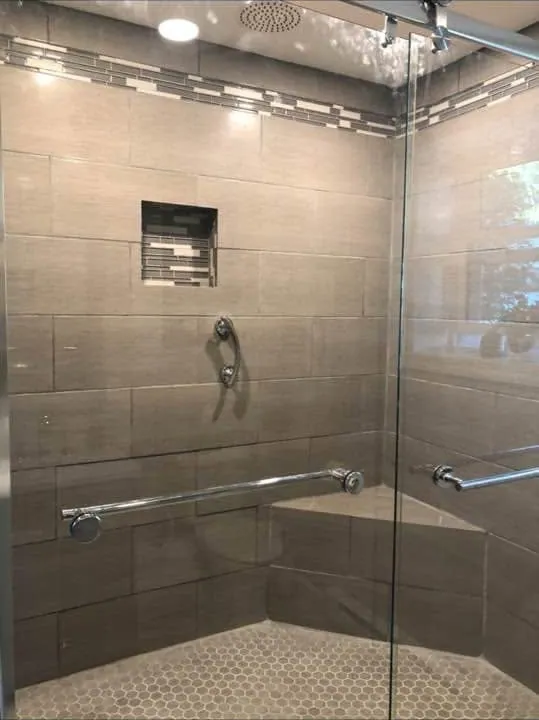 Tiled walk-in shower with a glass door, niche and corner bench